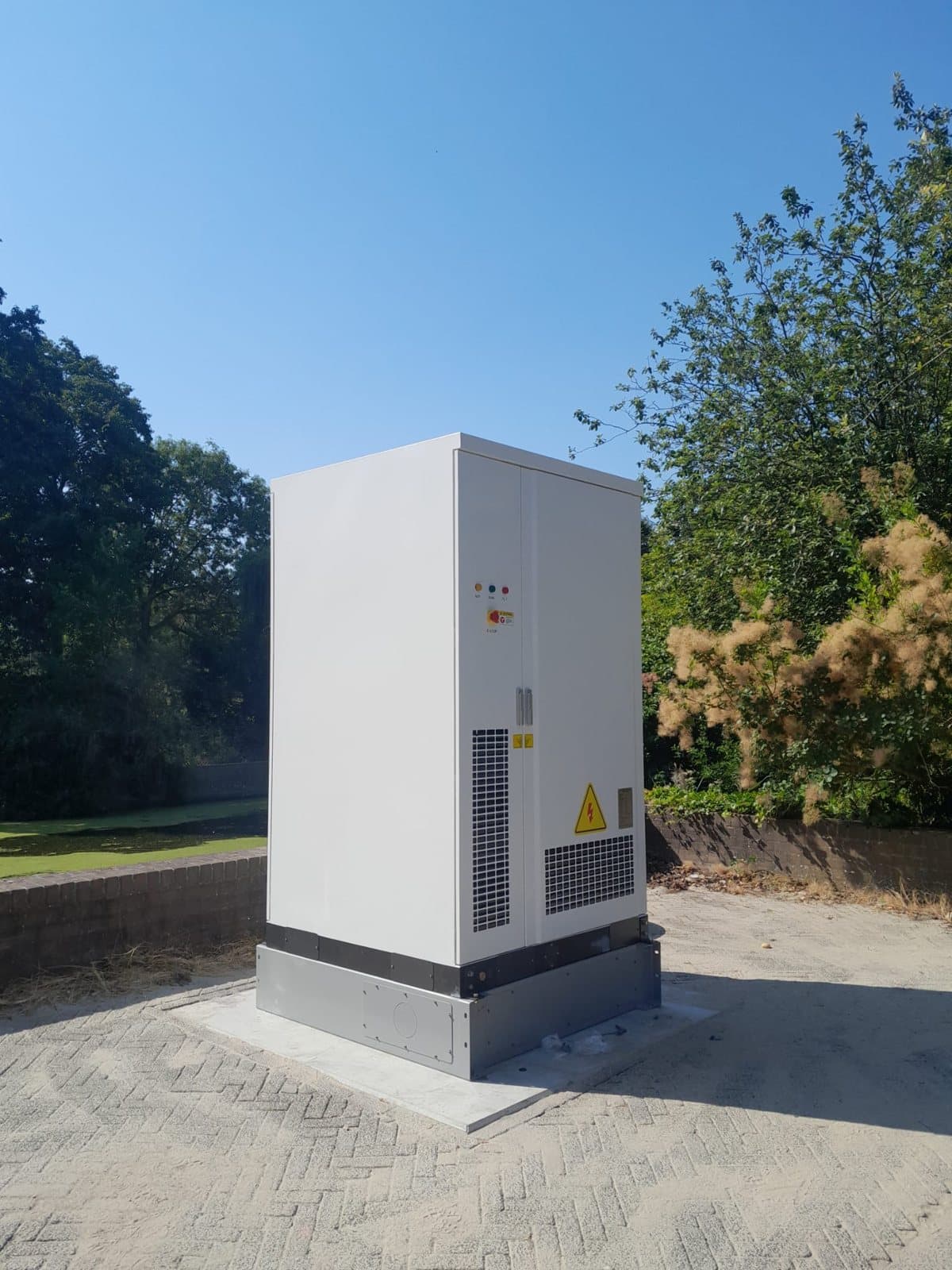 Eén batterijkast op een betonplaat, tussen bomen