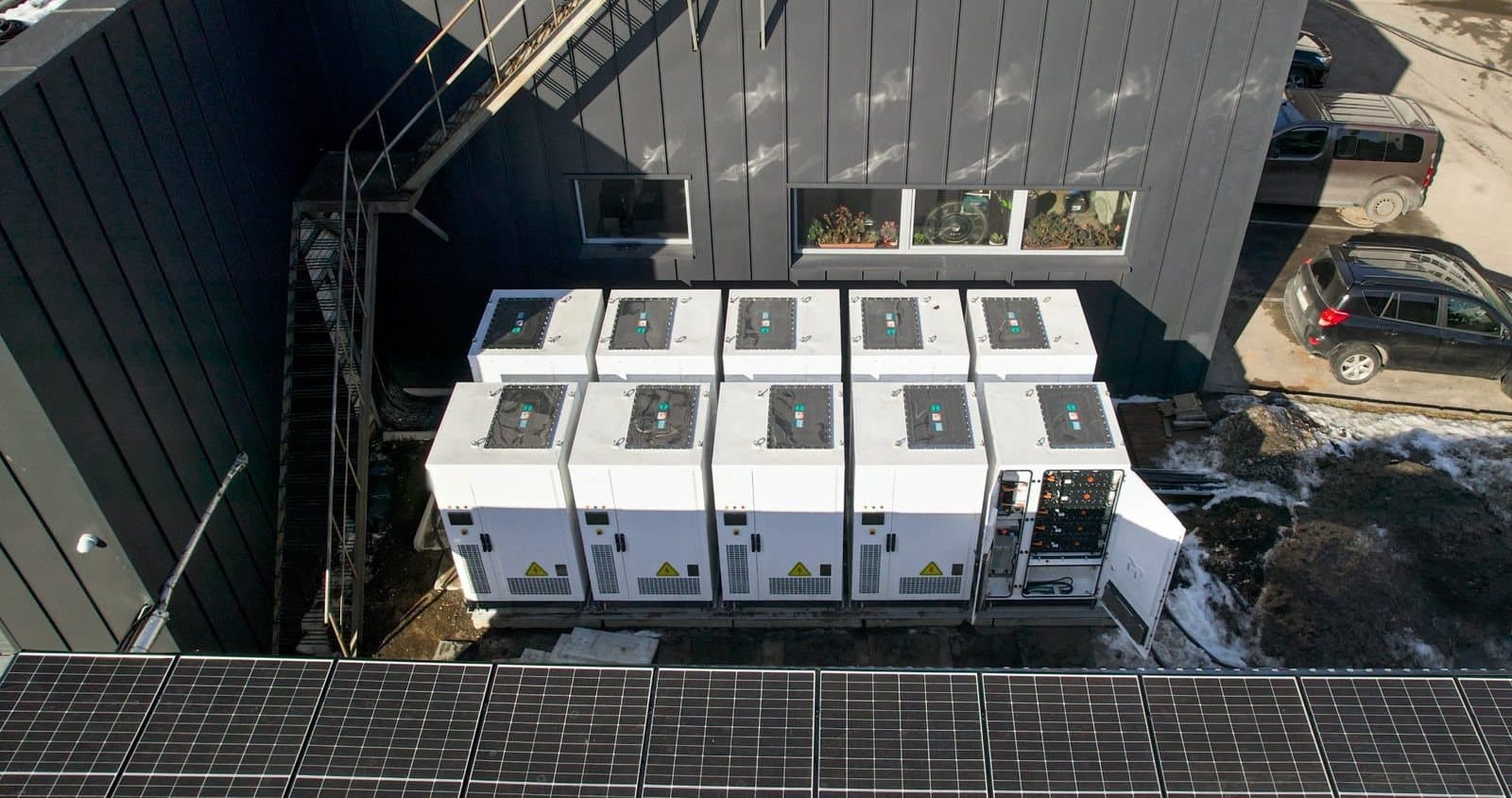 Tien batterijkasten van bovenaf gezien naast een bedrijfspand met zonnepanelen