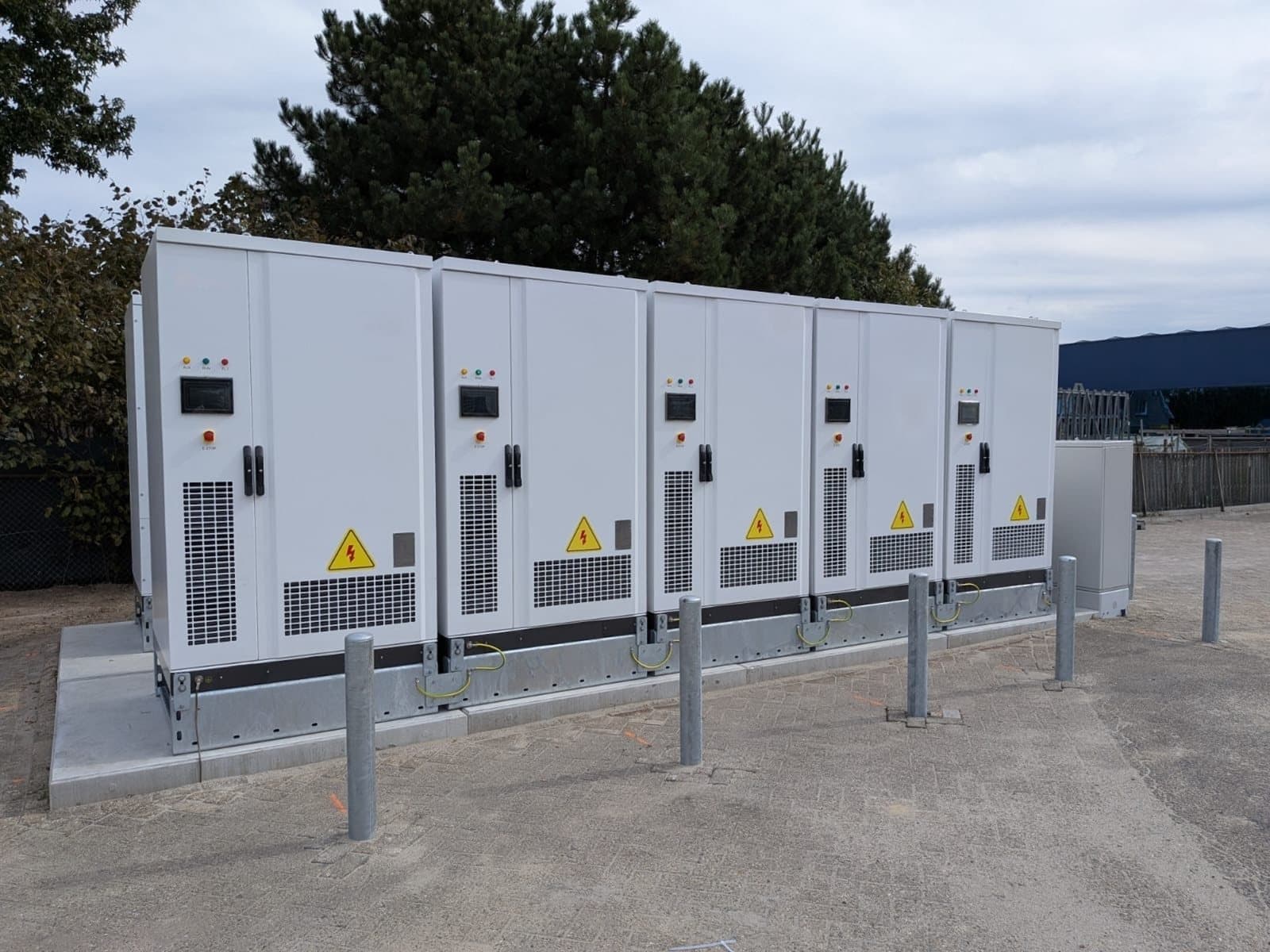 Een rij batterijkasten achter aanrijpalen op een bedrijfsterrein